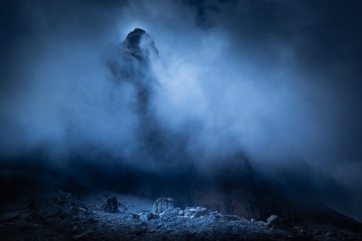 Guglia rocciosa tra la nebbia con rocce illuminate in basso, fotografia di paesaggio concettuale per il progetto The Dark Side.
