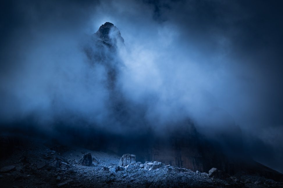 Guglia rocciosa tra la nebbia con rocce illuminate in basso, fotografia di paesaggio concettuale per il progetto The Dark Side.